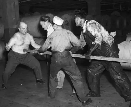 Frank being hit by a large piece of timber held by multiple men.