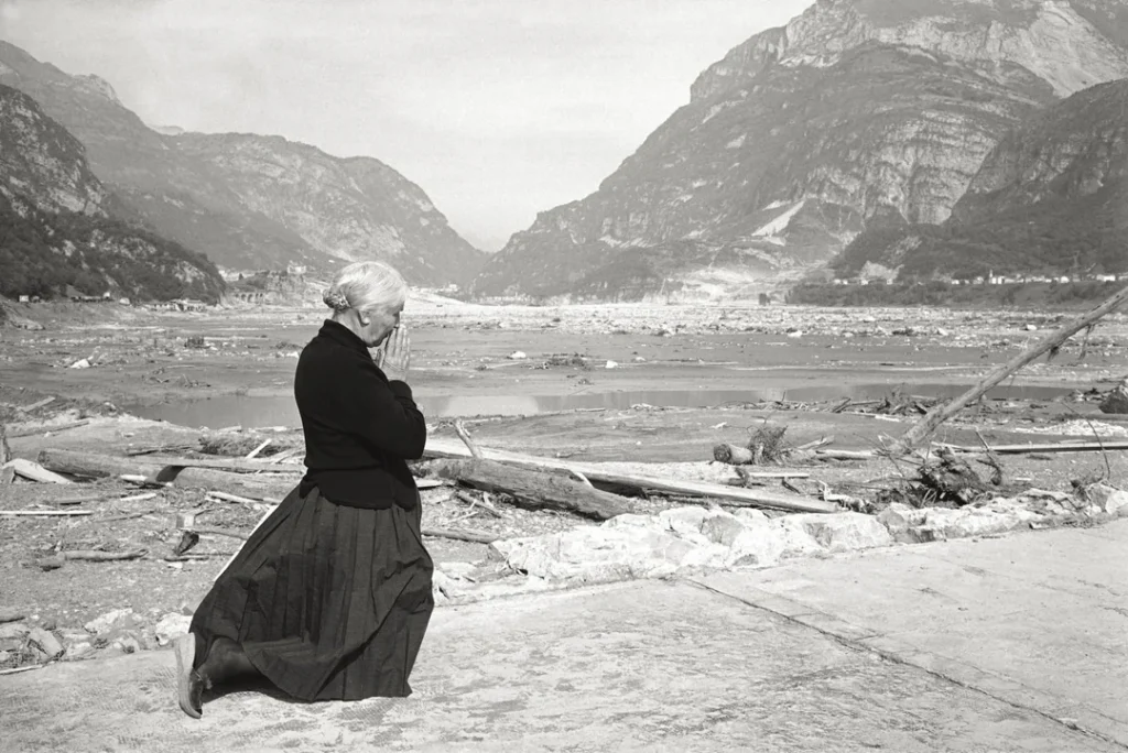 An elderly woman prays on the flat desert where a few hours earlier stood the parish church, swept away by the flood. On 9 Oct 1963, a landslide caused a giant wave to overtop the Vajont Dam, leading to the destruction of several villages and towns, killing over 2,000 (Longarone, Italy)
