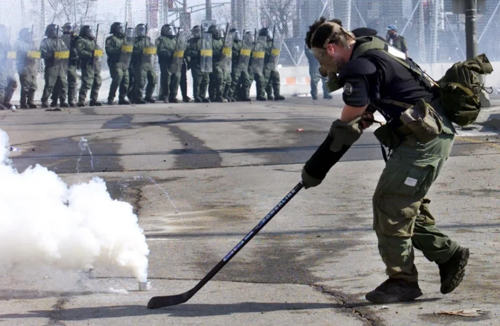 Canadian Protester uses a hockey stick to shoot tear gas canisters back at riot police during the 2001 Quebec City Protests