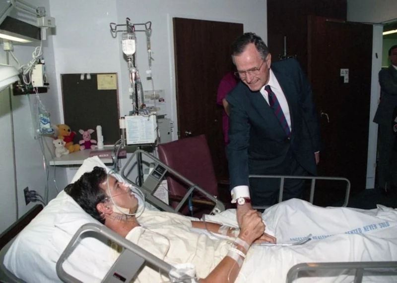 President George H. W. Bush makes a hospital visit to injured Los Angeles Fire Captain Scott Miller, who was shot in the face by a sniper while responding to one of many fires set during the first night of the Los Angeles riots (May 8, 1992)