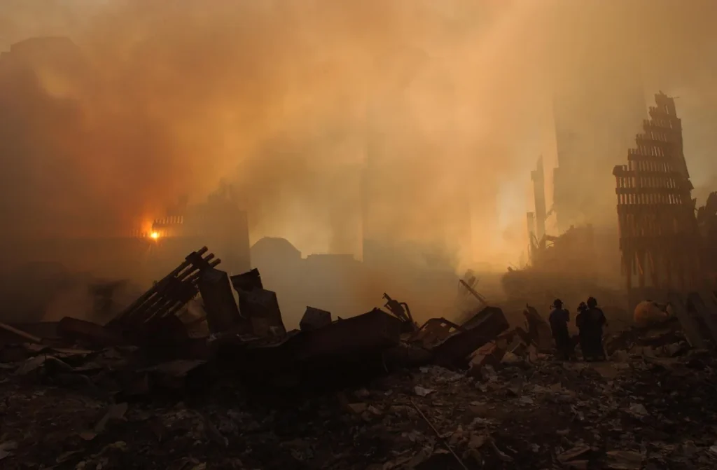 The sun streams through the dust and smoke over the wreckage of the World Trade Center as search and rescue efforts continue at ground zero. 13 September 2001