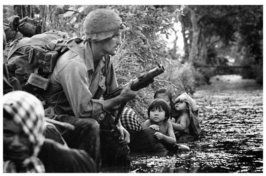 Two Vietnamese children, huddling against a canal bank for protection from Viet Cong sniper fire, gaze at an American paratrooper's M79 grenade launcher on New Year's Day, 1966, near Bao Trai.
